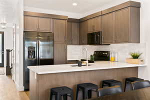 Kitchen featuring a peninsula, black appliances, a kitchen breakfast bar, tasteful backsplash, and light stone countertops