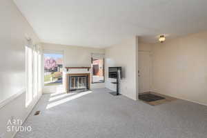 Unfurnished living room featuring a fireplace with flush hearth and light colored carpet