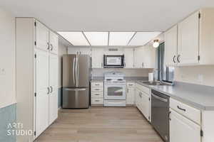 Kitchen with stainless steel appliances, light countertops, light wood-style flooring, and white cabinets