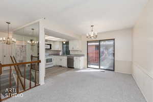 Kitchen with a chandelier, light colored carpet, white cabinetry, white appliances, and a wainscoted wall