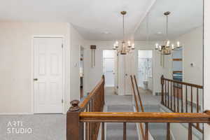 Corridor featuring an upstairs landing, light colored carpet, and suspended lighting