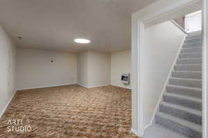 Finished below grade area featuring light carpet, heating unit, and a textured ceiling