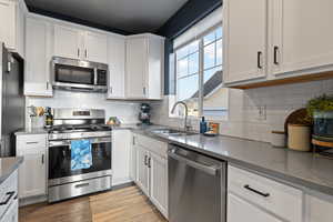 Kitchen with stainless steel appliances, white cabinets, backsplash, dark wood-style flooring, and dark stone countertops
