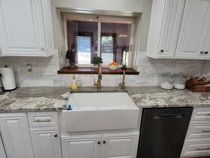 Kitchen featuring white cabinets, black dishwasher, light stone counters, and backsplash