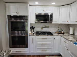 Kitchen featuring stainless steel appliances, white cabinetry, light stone counters, dark wood-style floors, and recessed lighting
