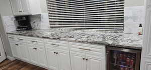Kitchen with dark stone counters, beverage cooler, white cabinetry, and dark wood finished floors