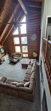 Carpeted living area with rustic walls, a high wooden beamed ceiling, and ceiling fan