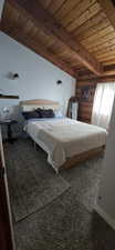 Bedroom with log walls, dark carpet, and a wooden ceiling with exposed beams