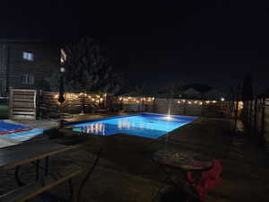 Pool at night with a fenced backyard and a patio area