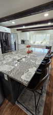 Kitchen with a kitchen breakfast bar, light stone counters, stainless steel fridge with ice dispenser, dark wood-style floors, and white cabinetry