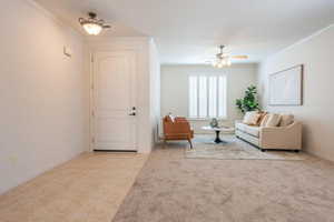 Living room with crown molding, light tile patterned floors, light colored carpet, and ceiling fan