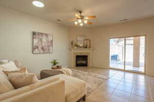 Living room with crown molding, a ceiling fan, light tile patterned flooring, and a tiled fireplace