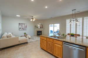 Kitchen with open floor plan, a tile fireplace, stainless steel dishwasher, light stone countertops, and decorative light fixtures