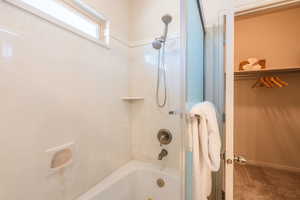 Bathroom featuring washtub / shower combination, a walk in closet, and carpet floors