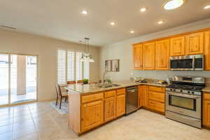 Kitchen with stainless steel appliances, a peninsula, light stone countertops, crown molding, and a chandelier