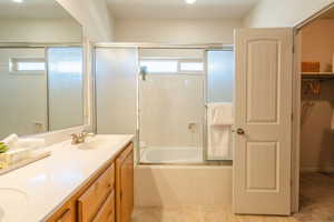 Full bath with enclosed tub / shower combo, a walk in closet, double vanity, and light tile patterned floors