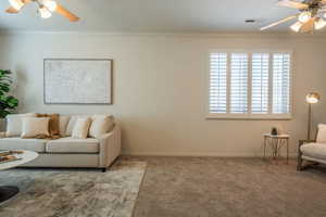 Living area featuring ceiling fan, carpet, and crown molding