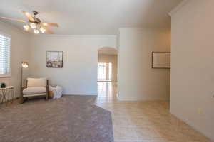 Living area with arched walkways, ornamental molding, ceiling fan, and light tile patterned floors