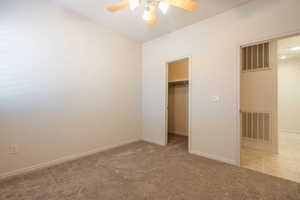 Unfurnished bedroom with light carpet, a walk in closet, ceiling fan, and vaulted ceiling
