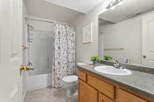 Full bathroom featuring vanity, shower / bathtub combination with curtain, and a textured ceiling