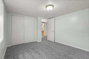 Unfurnished bedroom featuring a textured ceiling, carpet floors, and a closet