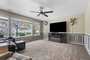Living room with a decorative wall, a ceiling fan, wainscoting, light carpet, and a textured ceiling