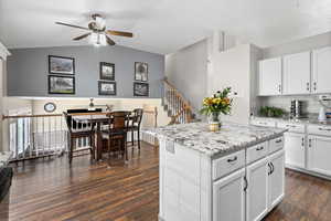 Kitchen with a ceiling fan, white cabinetry, light stone counters, a center island, and decorative backsplash
