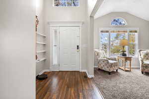 Entrance foyer featuring vaulted ceiling, dark wood finished floors, and dark colored carpet