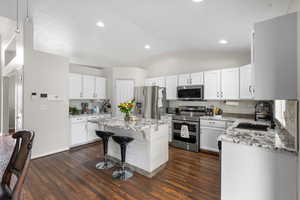 Kitchen featuring stainless steel appliances, a kitchen breakfast bar, light stone counters, white cabinets, and lofted ceiling