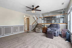 Living room with a decorative wall, a ceiling fan, a wainscoted wall, and carpet