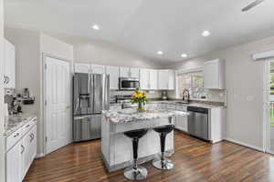 Kitchen featuring stainless steel appliances, a kitchen breakfast bar, light stone counters, a kitchen island, and vaulted ceiling