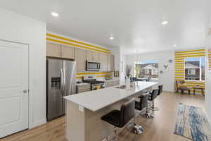 Kitchen featuring stainless steel appliances, an island with sink, a breakfast bar area, and light wood finished floors