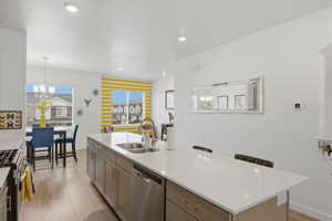 Kitchen featuring an island with sink, stainless steel appliances, light wood-style floors, a kitchen breakfast bar, and suspended lighting