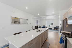 Kitchen featuring a kitchen island with sink, light wood-style flooring, stainless steel appliances, a breakfast bar area, and light stone countertops