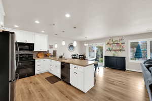 Kitchen featuring a peninsula, black appliances, white cabinets, decorative backsplash, and decorative light fixtures