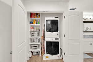 Laundry area with light wood-style floors and stacked washing machine and dryer