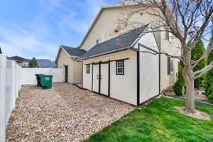 Back of house featuring a  large modern style shed, shingled roof, a fenced backyard, a gate, stucco siding, and a mountain view