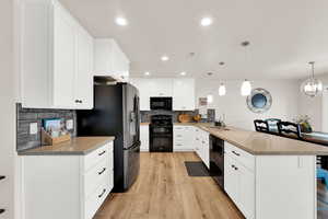 Kitchen with white cabinets, black appliances, light wood-type flooring, and a peninsula