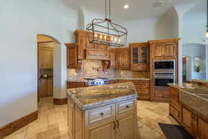 Kitchen with arched walkways, glass fronted cabinets, stainless steel appliances, stone tile floors, and a high ceiling