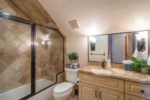 Bathroom featuring a textured wall, vanity, combined bath / shower with glass door, and a textured ceiling