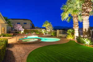 Pool at night with a pool with connected hot tub and a patio
