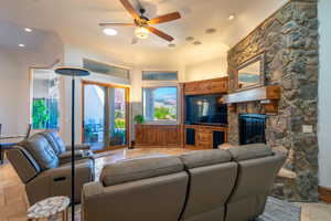 Living room featuring stone tile flooring, ceiling fan, a stone fireplace, and recessed lighting