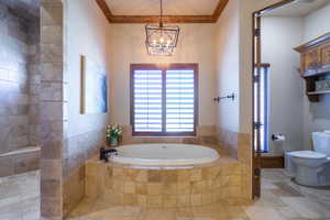 Full bath featuring stone tile flooring, ornamental molding, a garden tub, and suspended lighting