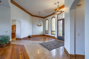 Foyer featuring arched walkways, hanging lights, crown molding, inlaid floor details, and light tile patterned flooring