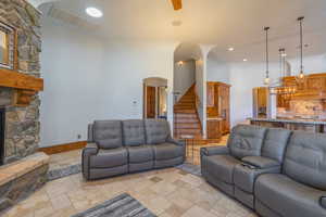 Living room featuring arched walkways, stone tile floors, a stone fireplace, recessed lighting, and a high ceiling