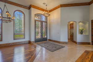 Foyer with hanging lights, ornamental molding, inlaid floor details, french doors, and arched walkways