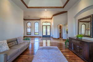 Foyer entrance with suspended lighting, crown molding, dark wood finished floors, and arched walkways