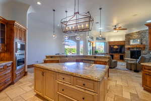 Kitchen with a stone fireplace, stone tile flooring, ceiling fan, and open floor plan