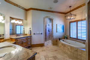 Full bathroom featuring suspended lighting, a garden tub, two vanities, ornamental molding, and stone tile flooring