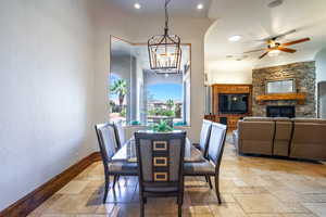 Dining space with stone tile flooring, ceiling fan, a fireplace, a textured wall, and a chandelier